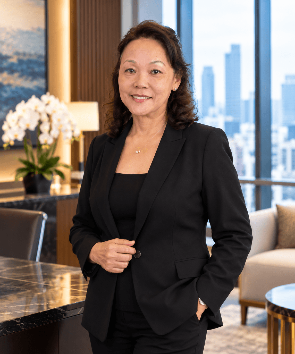 Smiling professional woman in a black blazer standing in a modern office with city skyline views.